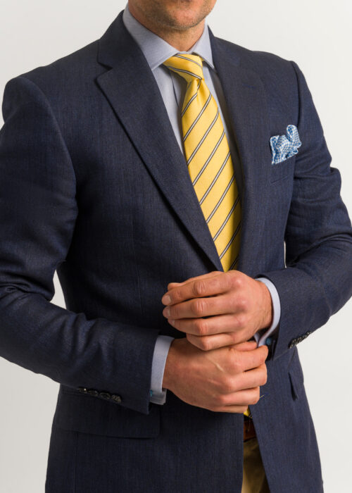 A beautifully cut men's navy herringbone linen jacket, styled with yellow silk tie and sky blue pocket square.