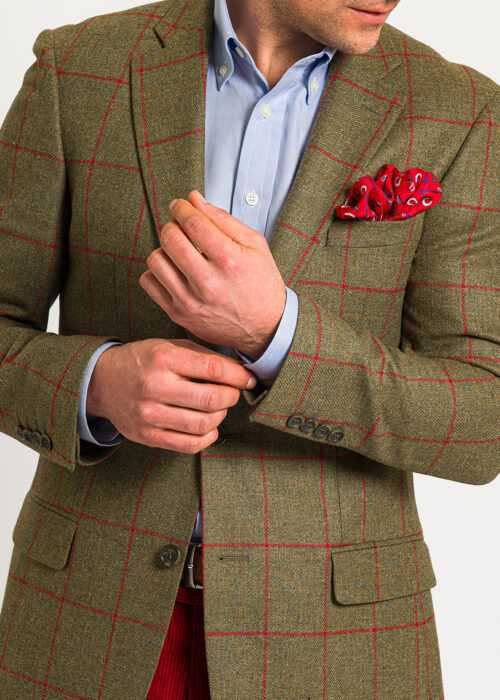 A men's tan wool jacket with red check. styled with blue open neck shirt and red pocket square.